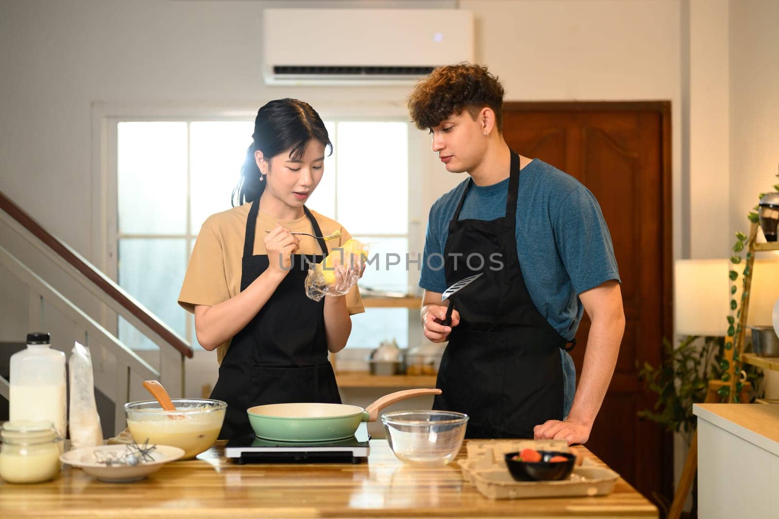 Man and woman in aprons starting to make pancakes in cozy home kitchen.