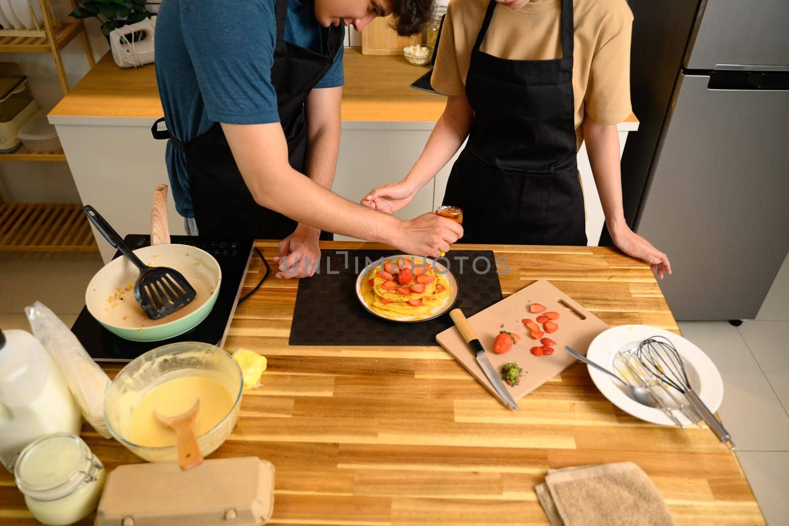 Loving young couple decorating homemade pancakes with sliced strawberries together.