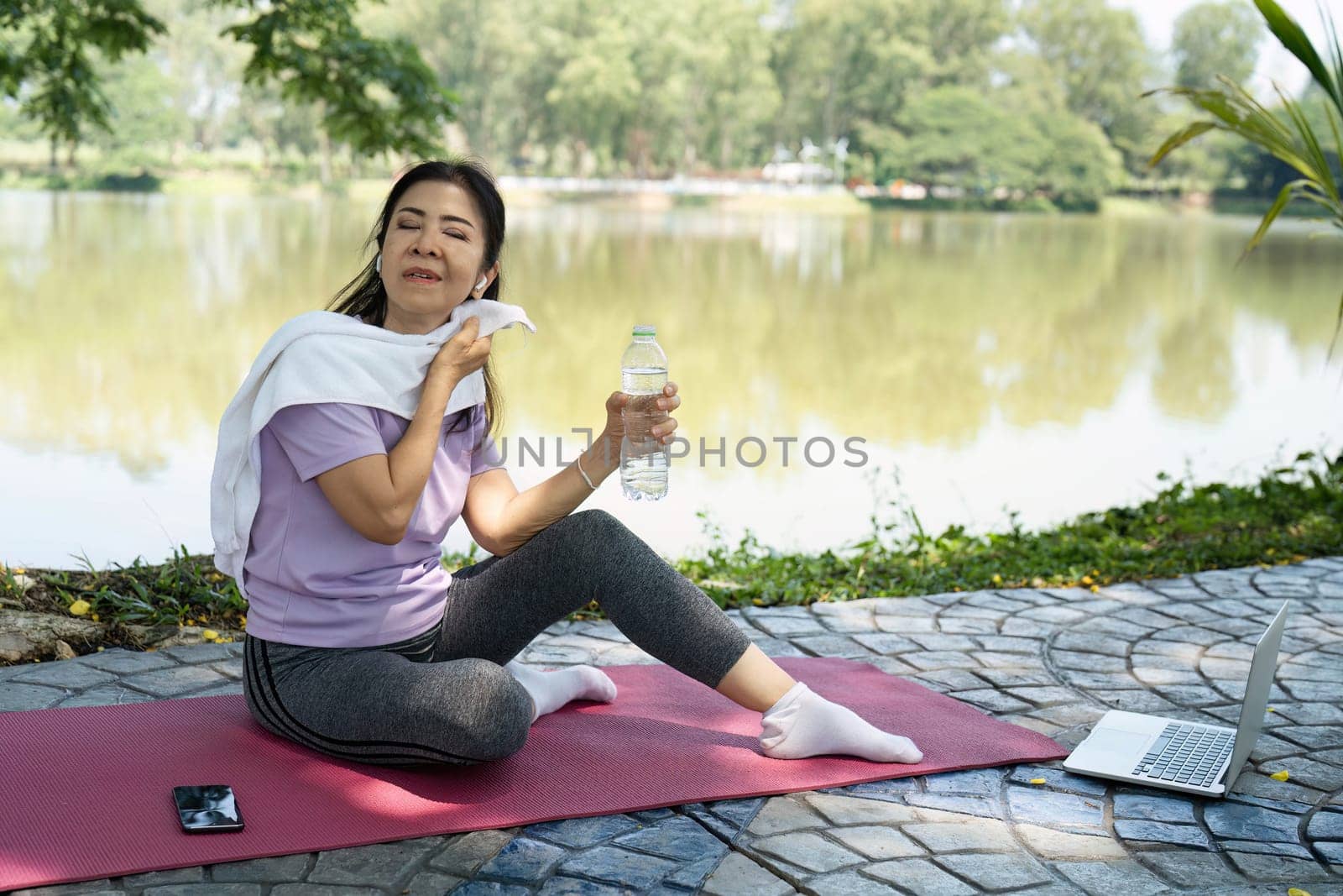 A woman wipes her sweat and drinks water after yoga, emphasizing wellness and hydration in nature.