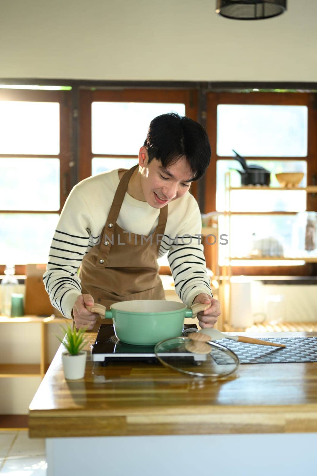 Young man smiling while preparing food in a home kitchen, standing over a pot on the stove.