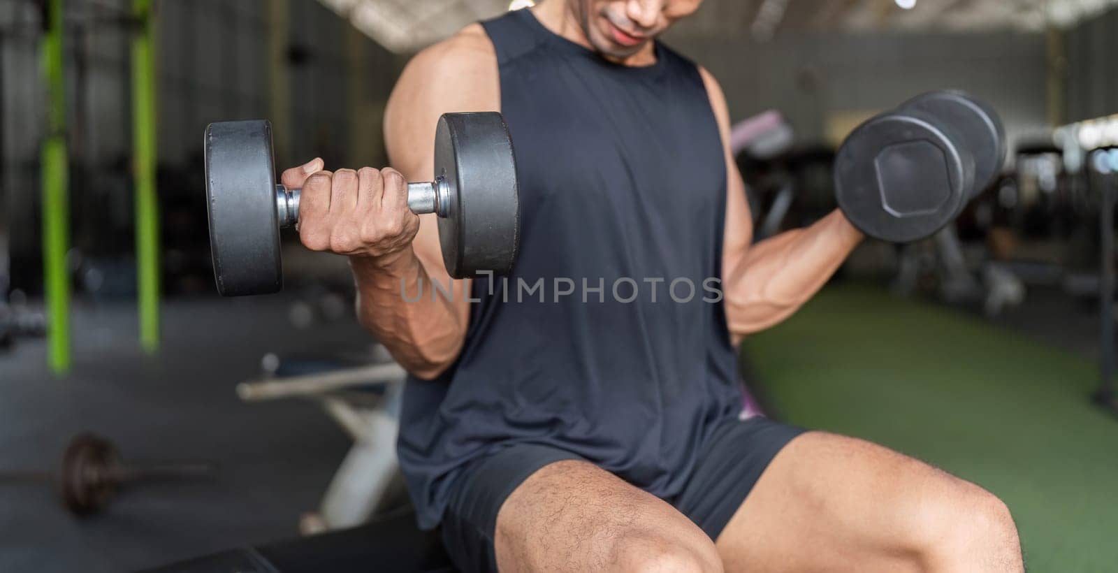 A dedicated young man engages in strength training by performing bicep curls with dumbbells in a modern gym environment.