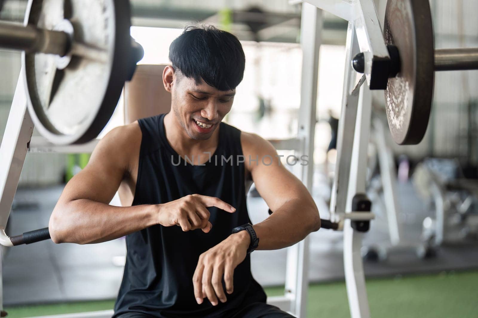 A young man checks his fitness tracker on his wrist while sitting in a gym, highlighting technology's role in modern fitness.