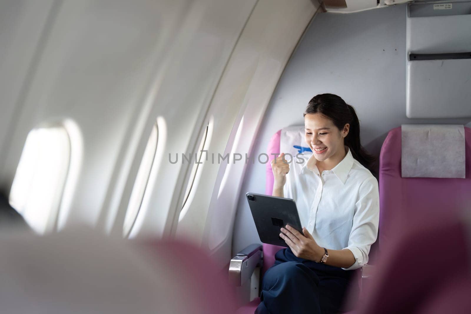A joyful businesswoman celebrates a success on her tablet while flying, highlighting the blend of work and happiness.