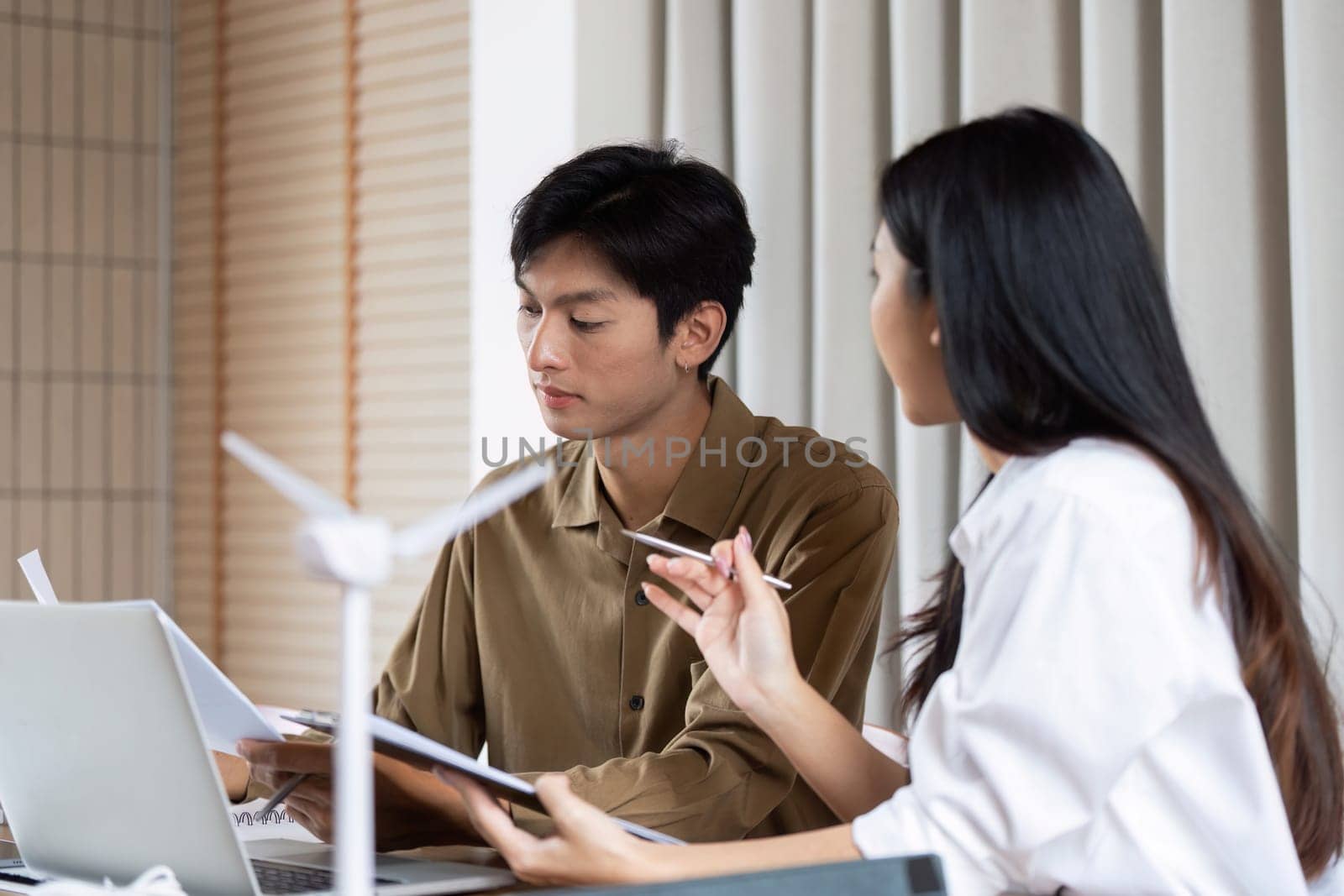 A business meeting focused on green technology, showcasing a man and woman collaborating on eco-friendly projects with wind turbine models in view.