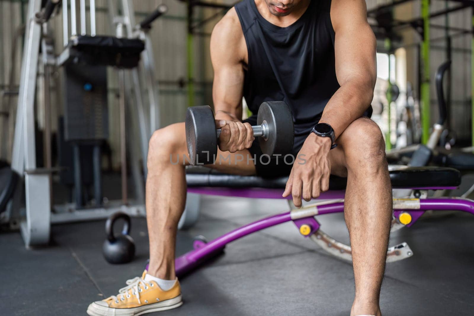 A young man focuses on his form while performing a dumbbell curl, emphasizing strength training and fitness dedication.