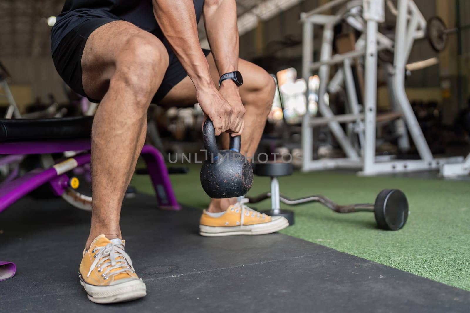 A young man demonstrates strength and focus while lifting a kettlebell in a gym, emphasizing his commitment to fitness.
