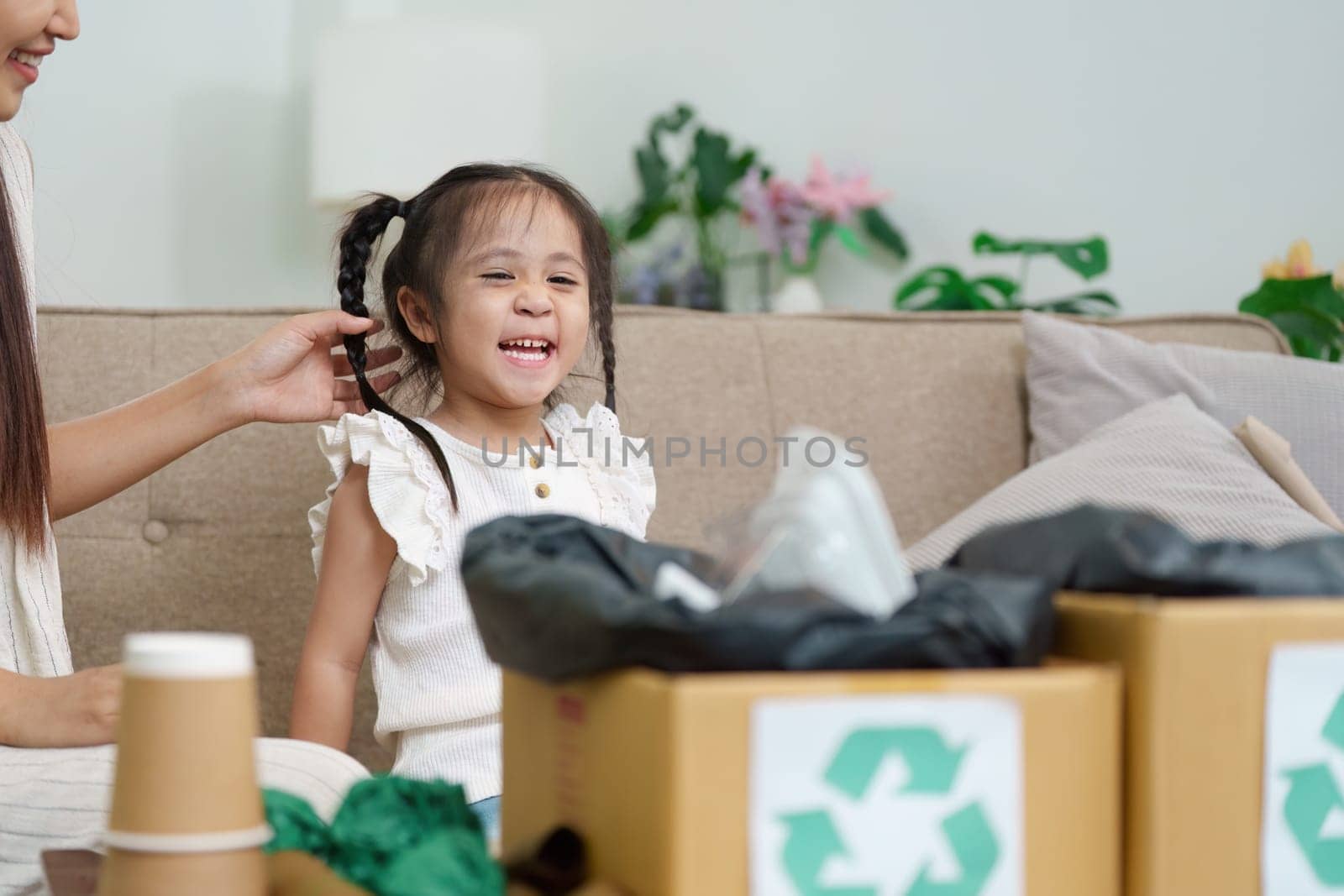 A playful moment occurs as one girl participates joyfully in a recycling project, helping her family sort materials in their living room.