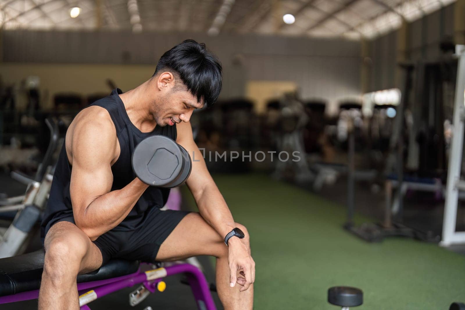 A man focuses on his form while lifting a dumbbell in a gym, highlighting his commitment to strength training.