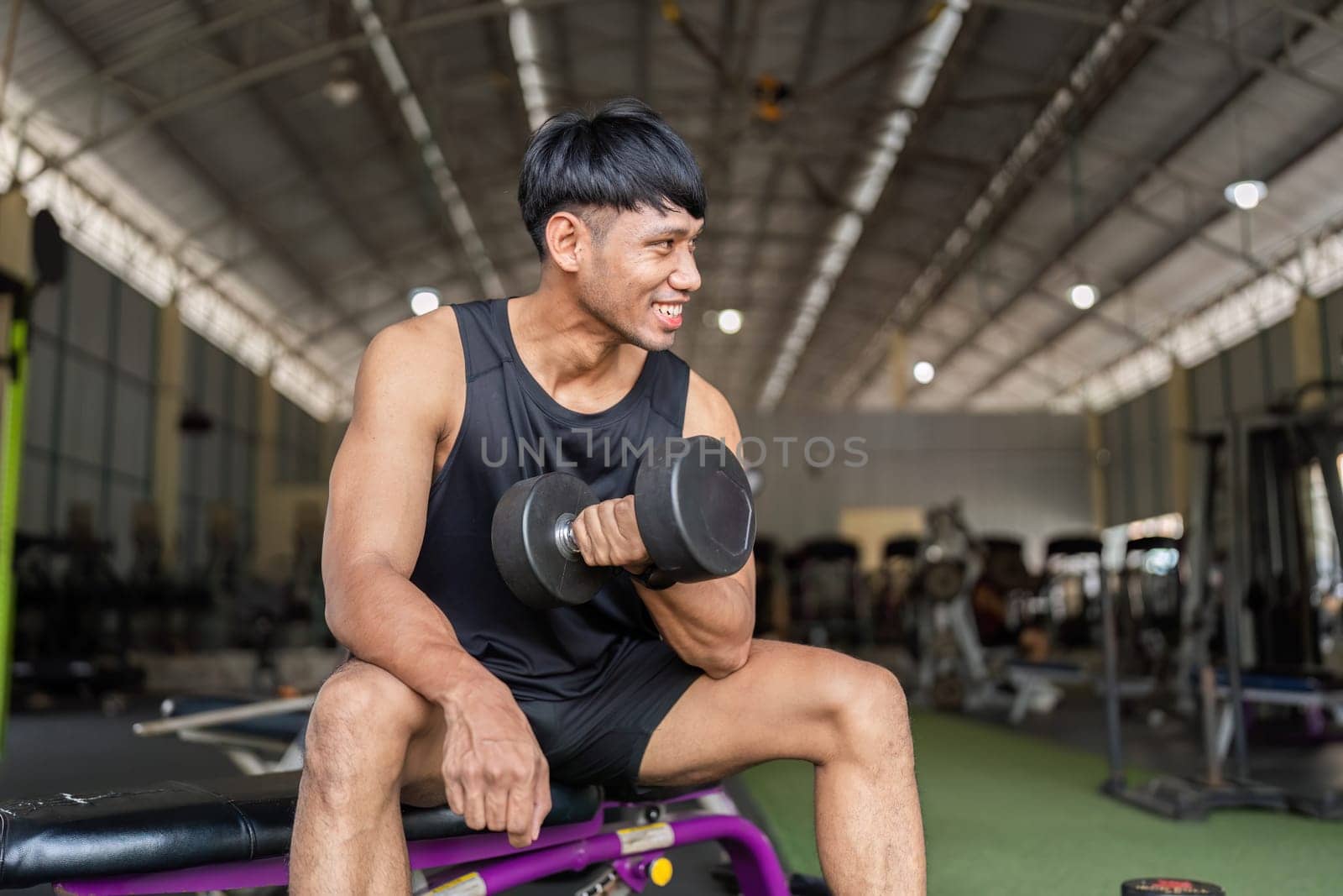 A young man smiles while lifting a dumbbell, showcasing a positive attitude towards fitness and strength training.