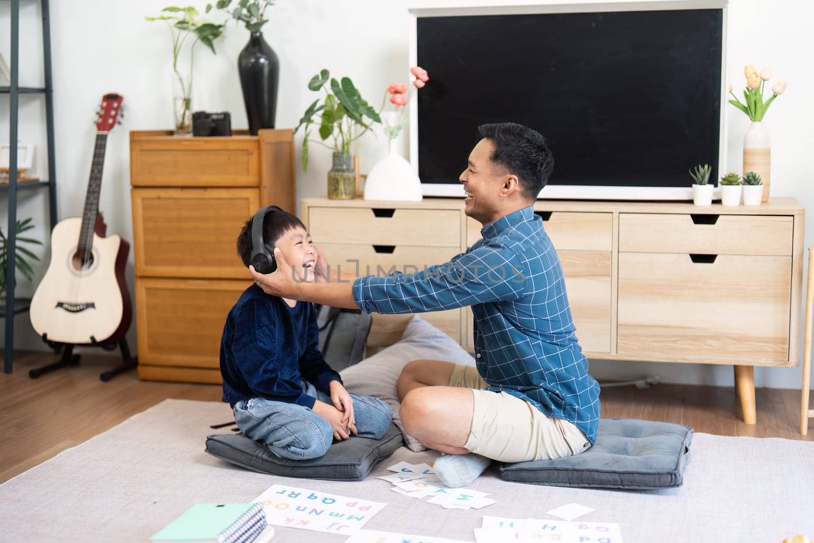 A father and son share a light-hearted moment while studying with headphones, emphasizing fun in education at home.