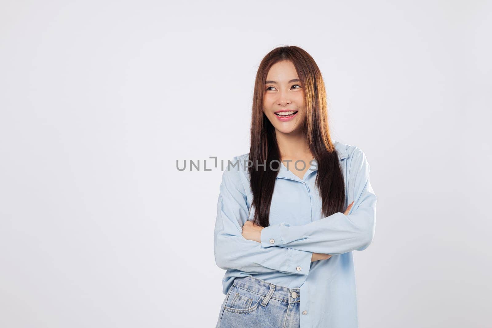 Asian woman posing confidently with crossed arms, expressing positivity and power with crossed arms and warm smile against isolated white backdrop.