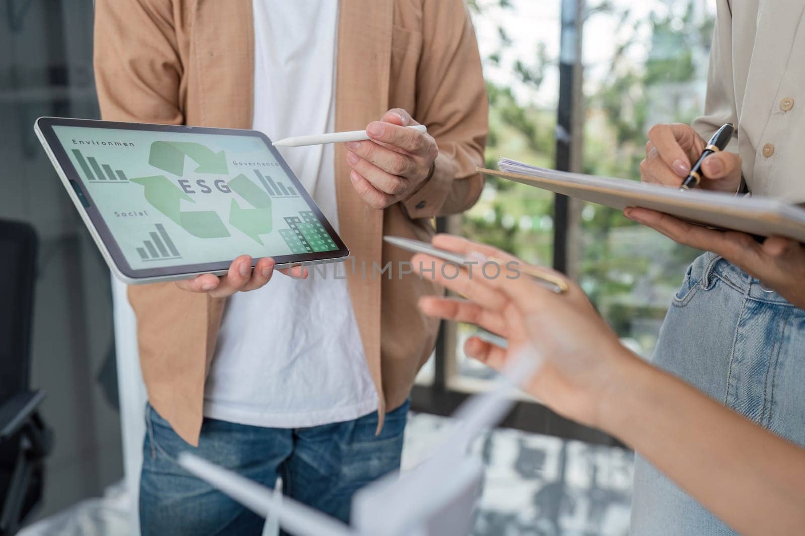 Team members discussing ESG metrics and sustainable practices while reviewing data on digital devices in a modern office setting.