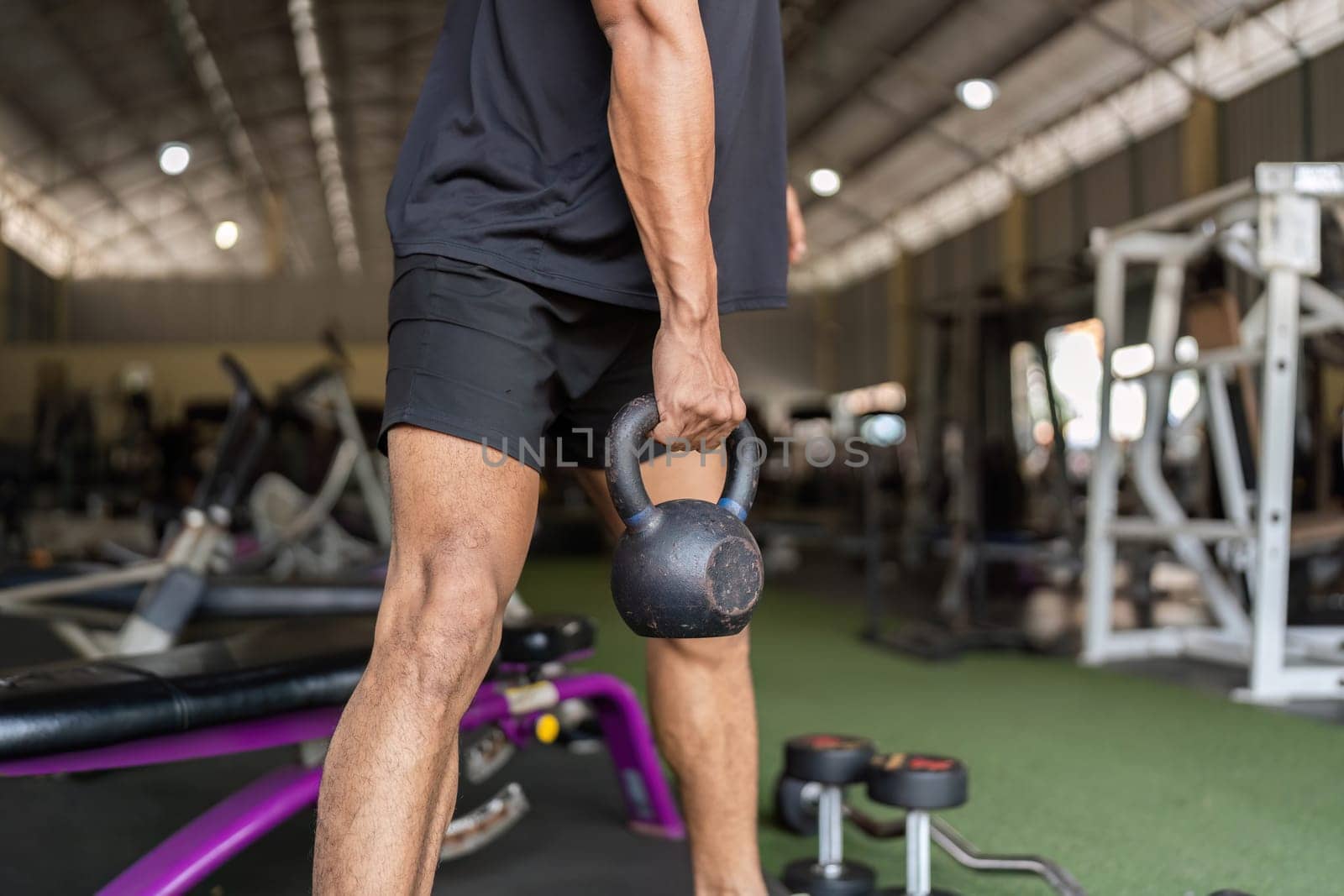 A focused individual engages in strength training, lifting a kettlebell in a well-equipped gym, showcasing determination and fitness.