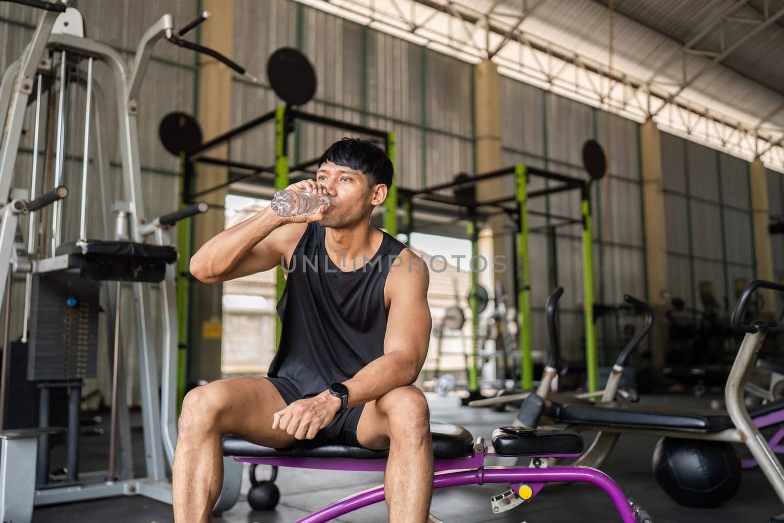 A man takes a refreshing drink of water after an intense workout session in the gym, emphasizing hydration and health.