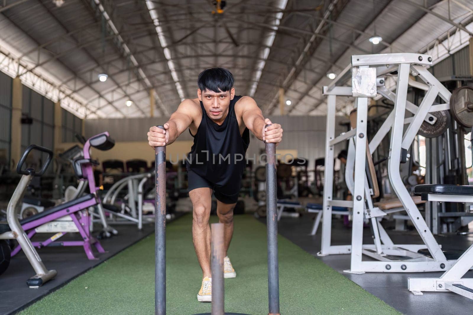 A young man pushes a weighted sled in a gym, demonstrating strength, endurance, and commitment to fitness.