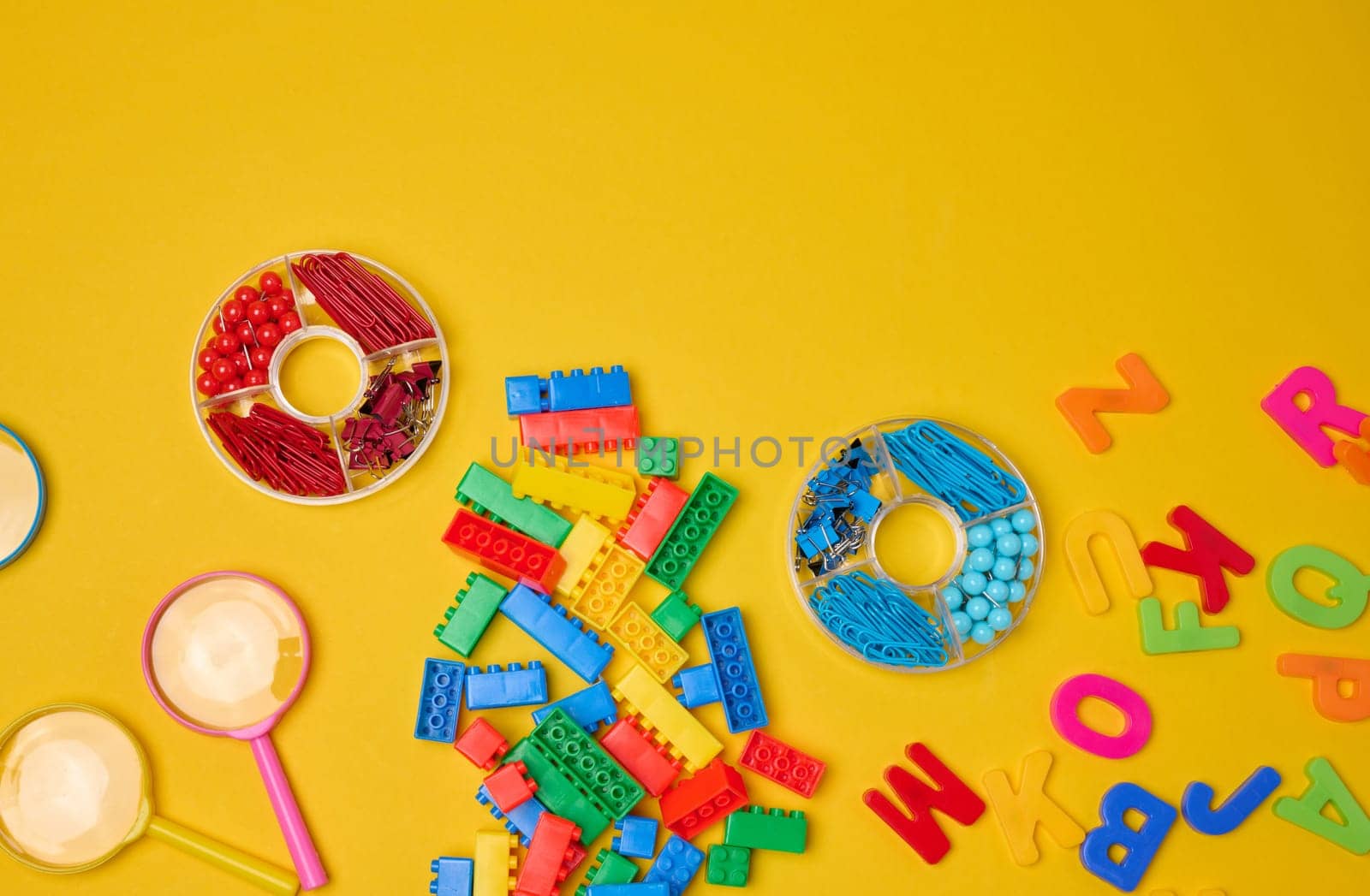 Collection of colorful school supplies, building bricks, letters, and learning items scattered on a yellow background. Play and education concept.