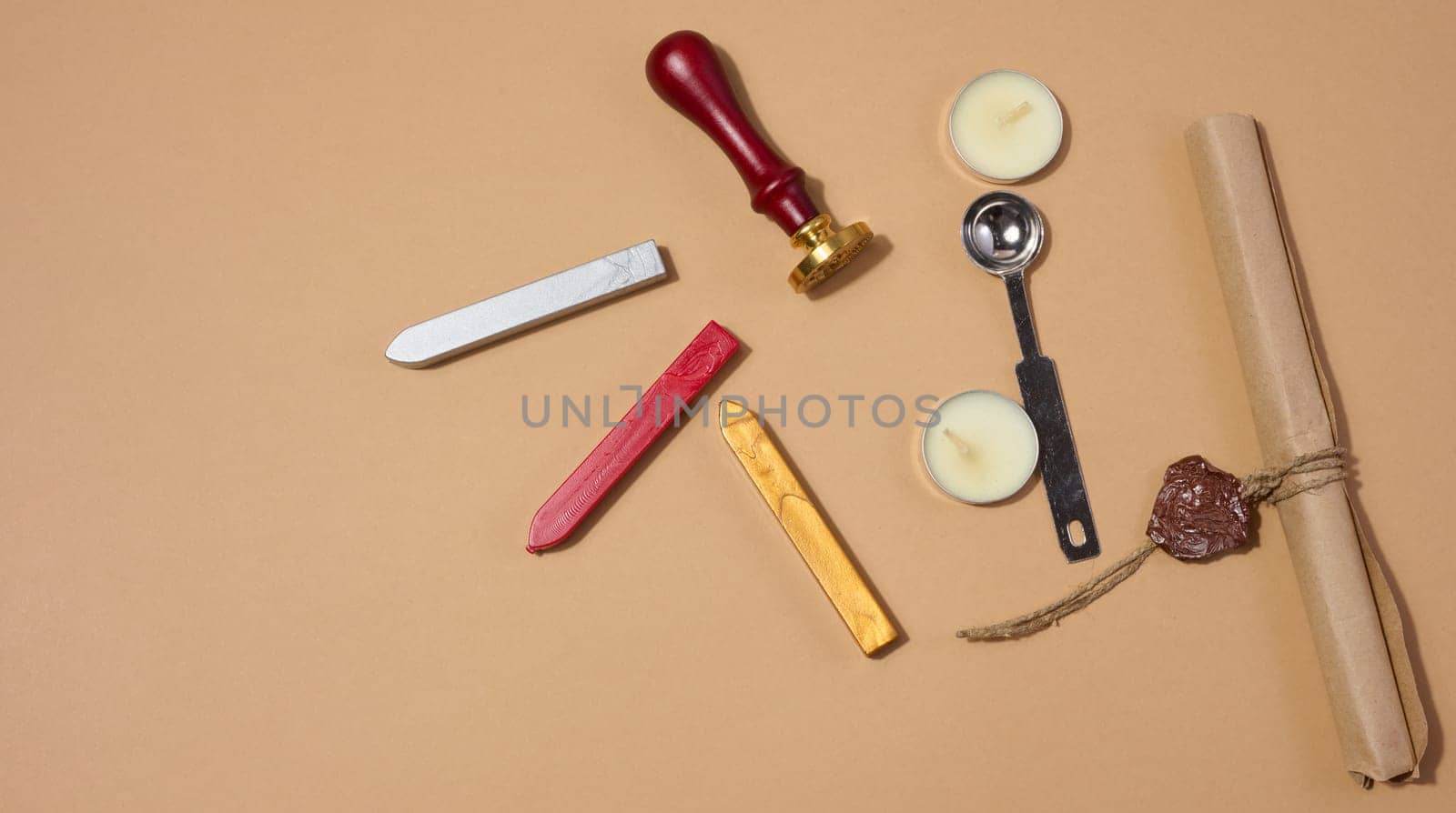 A wax seal kit including wax sticks, spoon, candles, stamp and sealed scroll placed on a neutral background