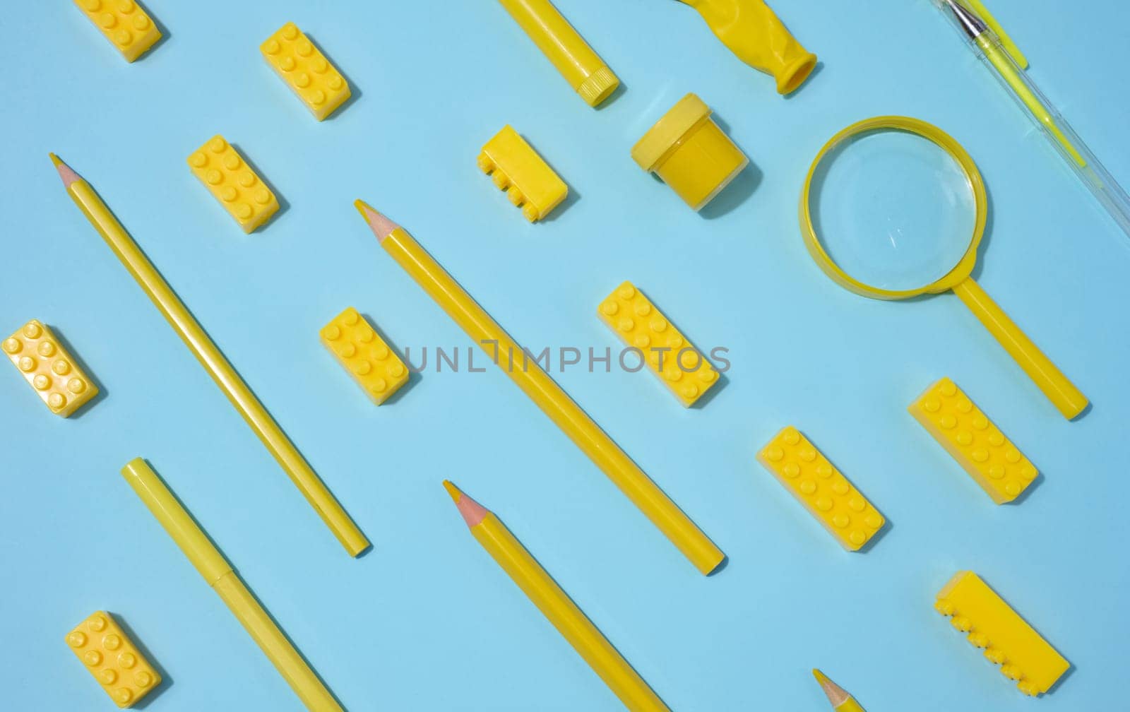 Various yellow objects including pencils, magnifying glass and toy blocks scattered on blue background, top view