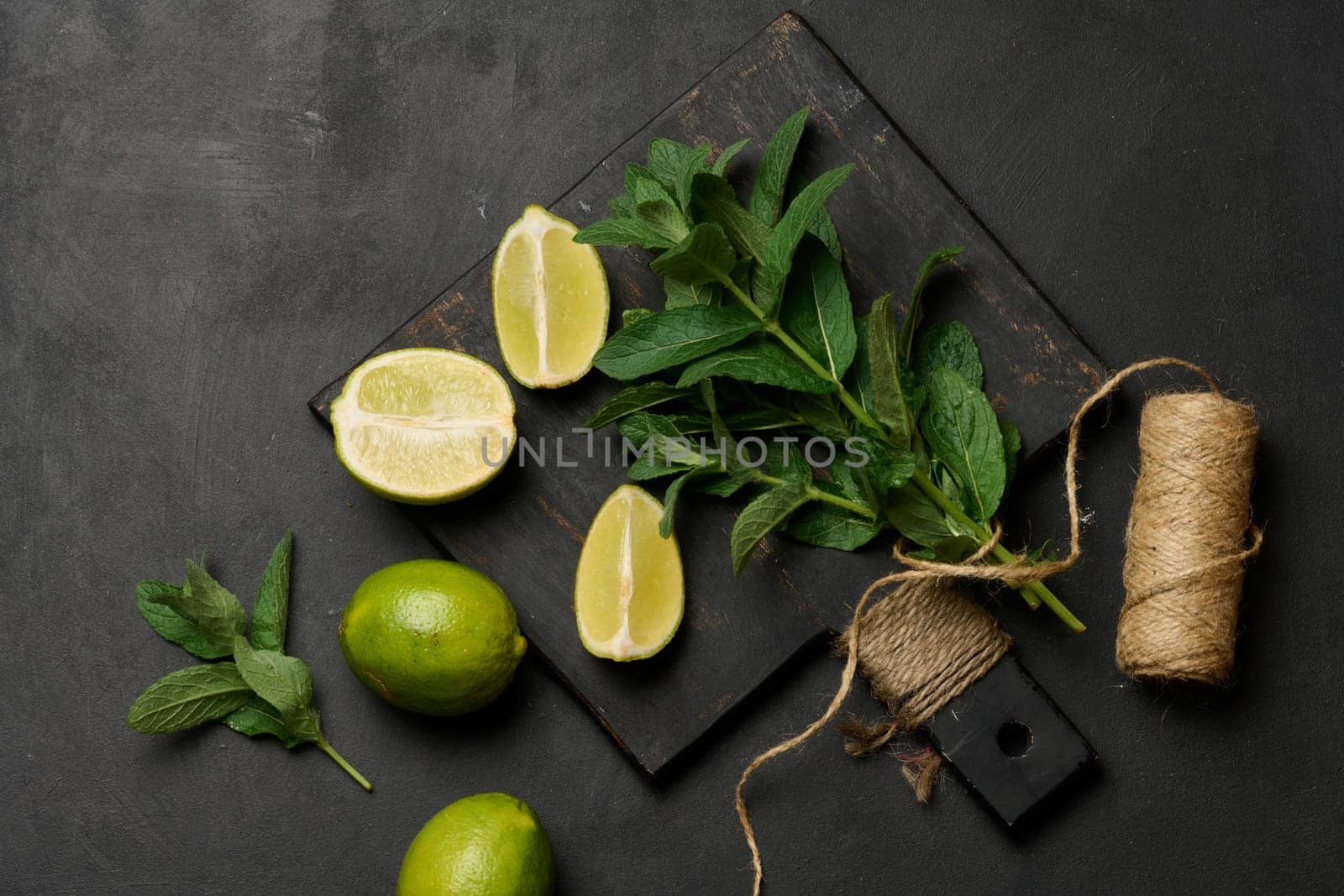 Bunch of fresh green mint and lime wedges on wooden board, top view