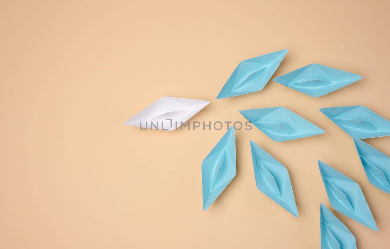 One white origami paper boat leads a group of blue boats on a neutral background