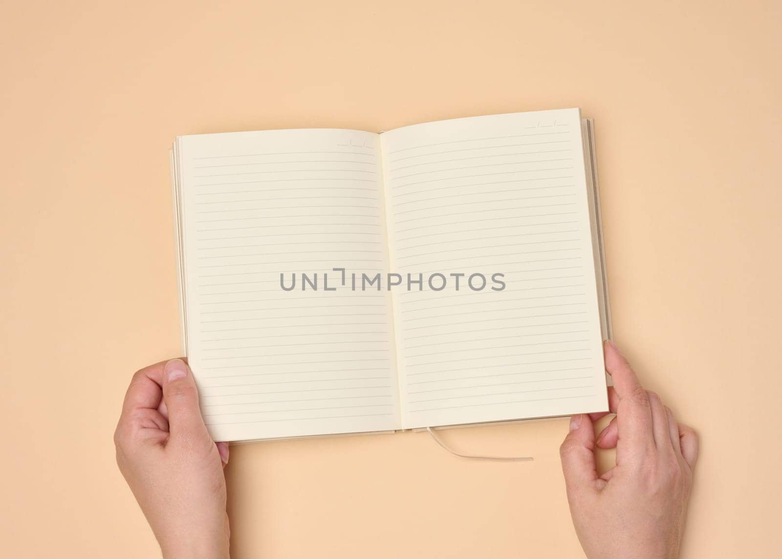 Hands hold a blank open notebook on a neutral background, top view