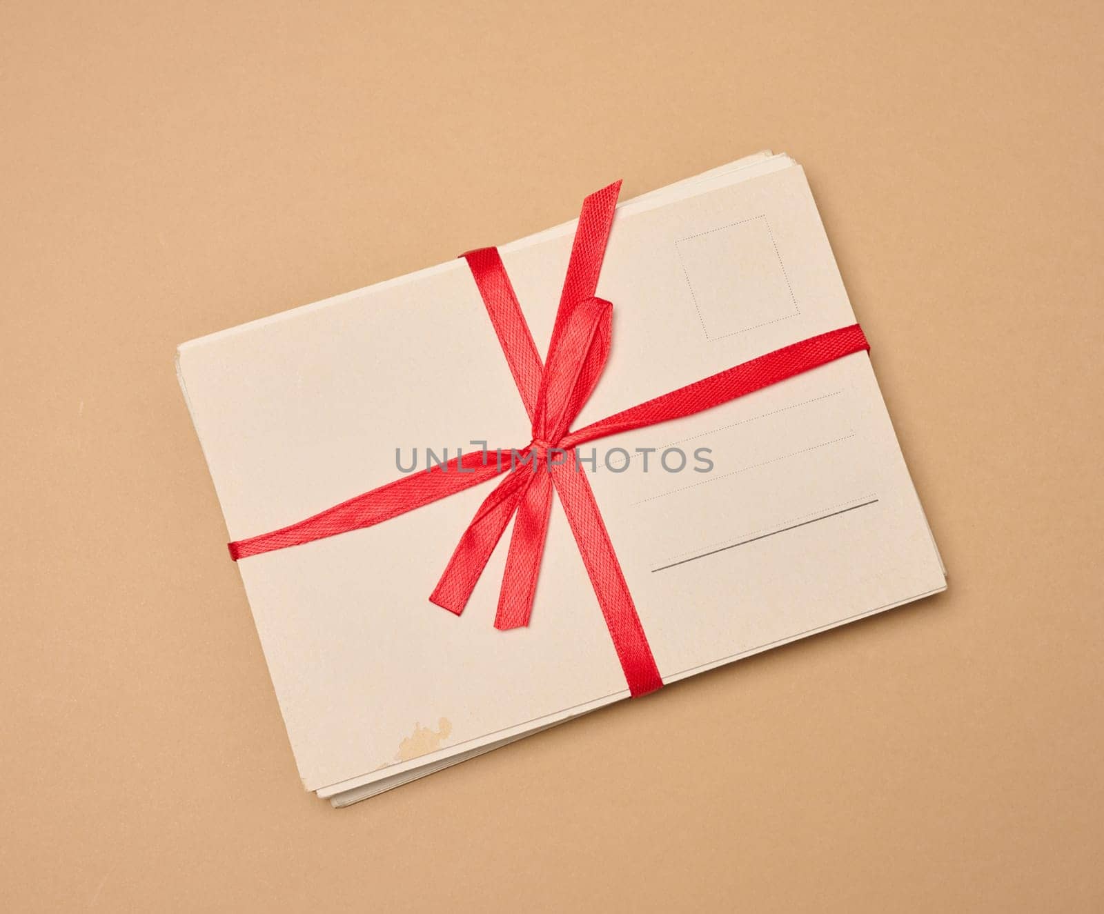 A stack of blank postcards tied with a red ribbon and bow lies on a neutral background.