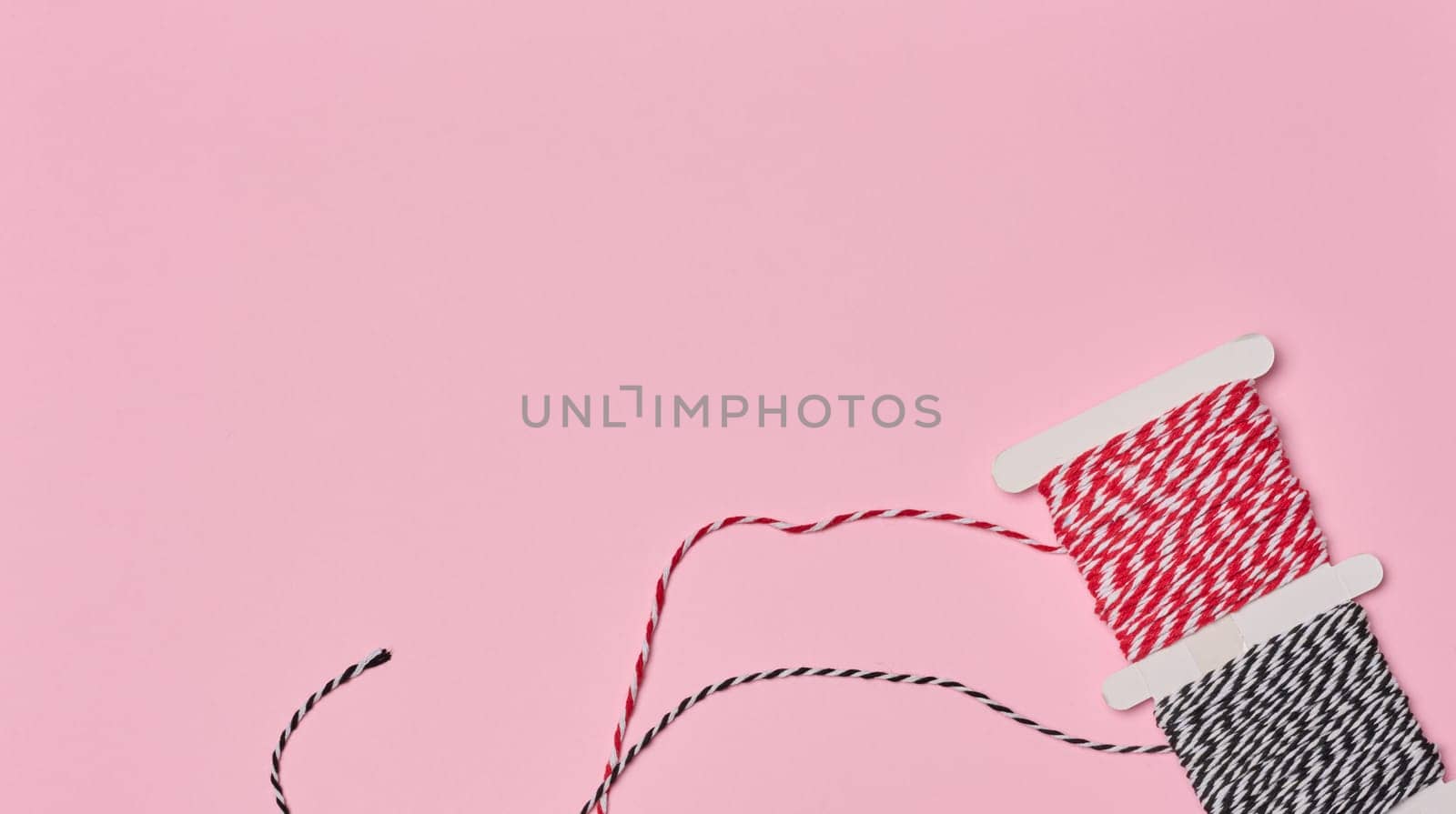 Two spools of red and white and black and white striped twine on a pink background.