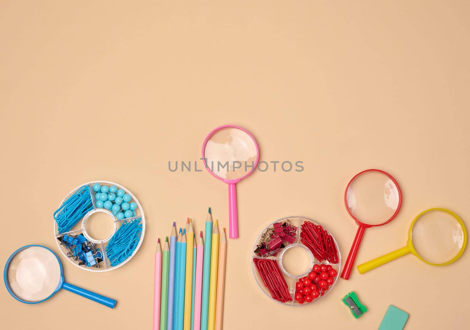 Various office and school supplies, including pencils, magnifying glasses, paper clips and pins, are neatly arranged on a neutral background.