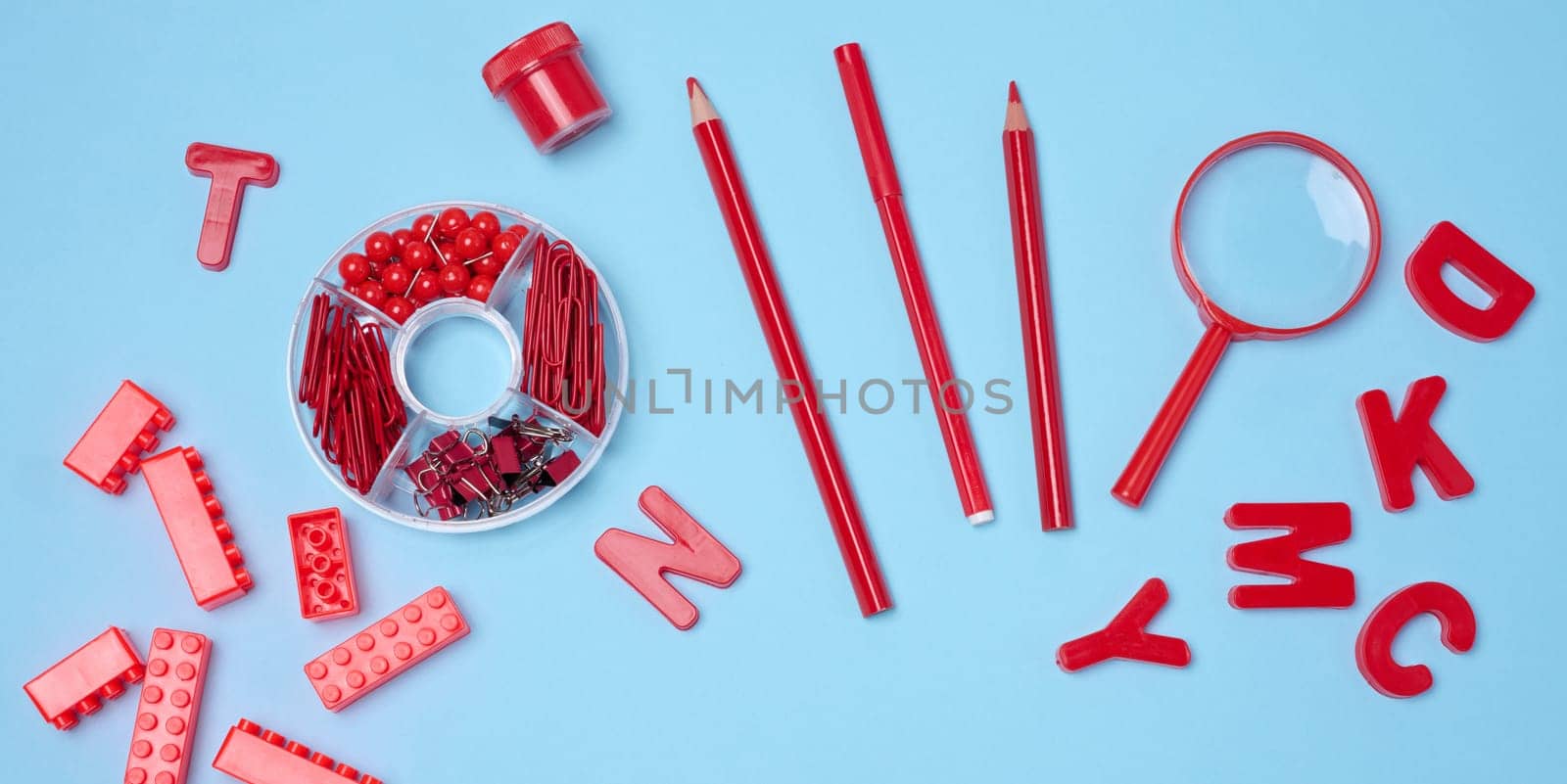 Flat lay of red stationery, learning items letters, magnifying glass, supplies, bricks, toys, and alarm clock on a light blue background. Education, time, and study concept.