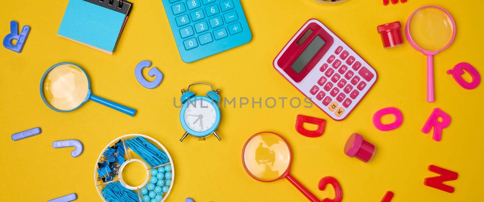 Colorful school supplies, learning items calculators, letters, tools, and stationery scattered on a vibrant yellow background. Education and back to school concept