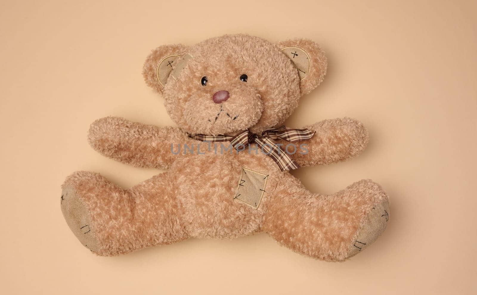 Fluffy brown teddy bear with a ribbon lying on a neutral background, top view