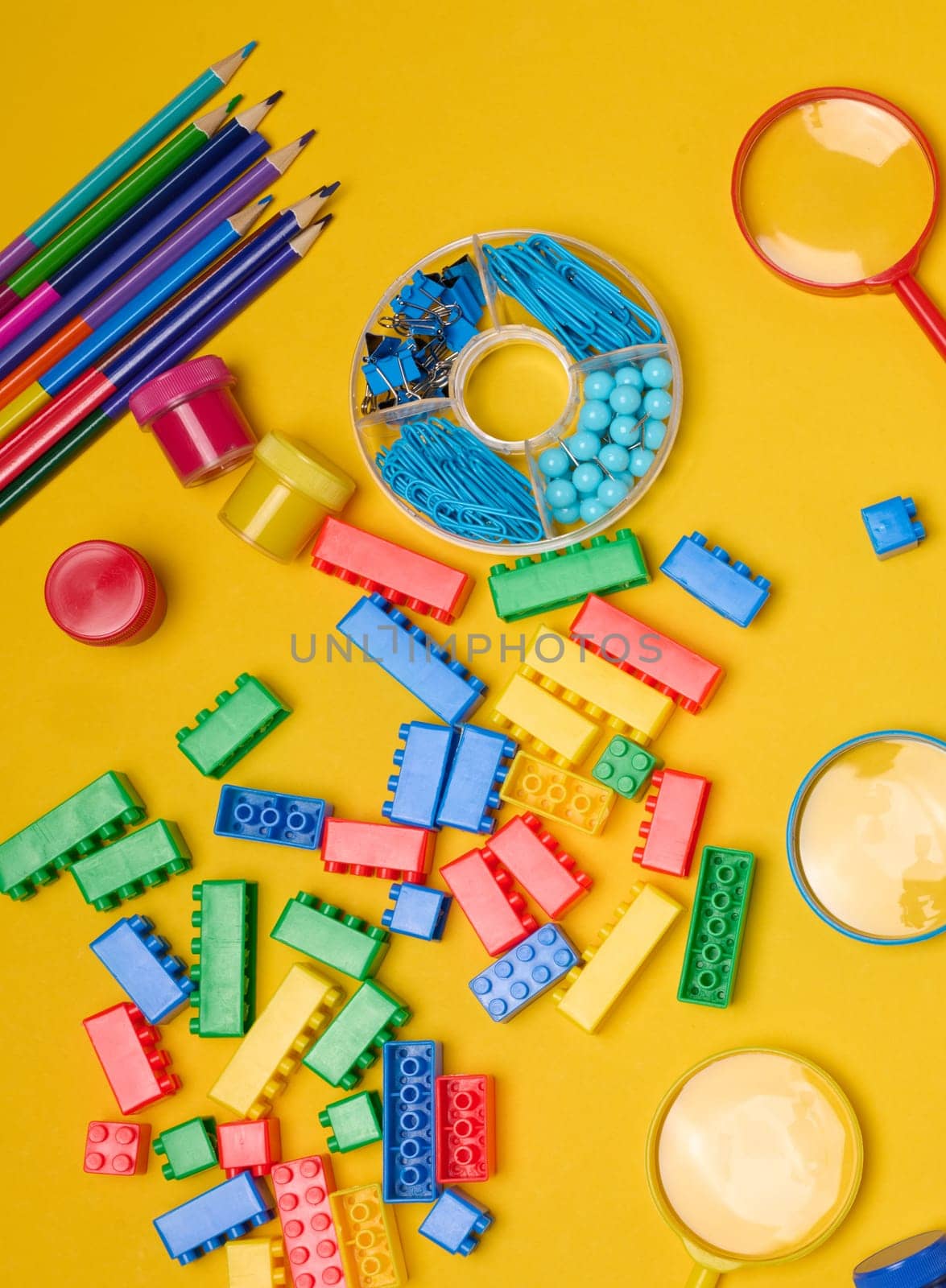 Vibrant collection of colorful school supplies, building bricks, letters, and learning items scattered on a yellow background. Play and education concept.