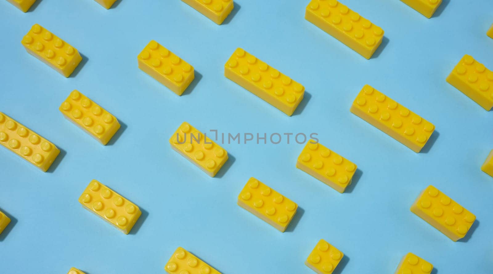 Scattered yellow plastic toy building bricks on a blue background. Play, construction, education or creative concept
