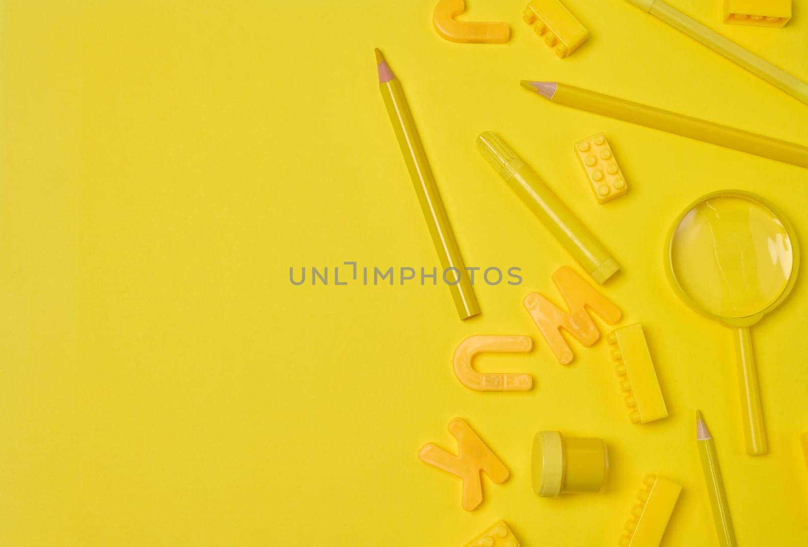 Assortment of yellow stationery and creative items scattered on a yellow background. Pencil, marker, building brick, letter, magnifying glass. Education or art concept
