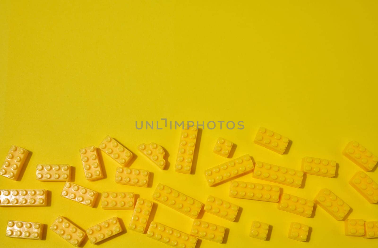 Scattered yellow plastic toy building bricks on a solid yellow background. Play, construction, education or creative concept