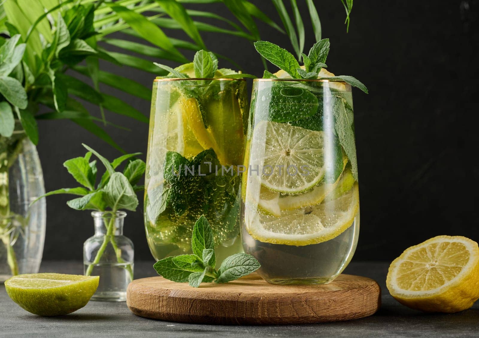 Refreshing detox or summer drink in a glass with lemon, lime, mint, ice, and metal straw. Dark background