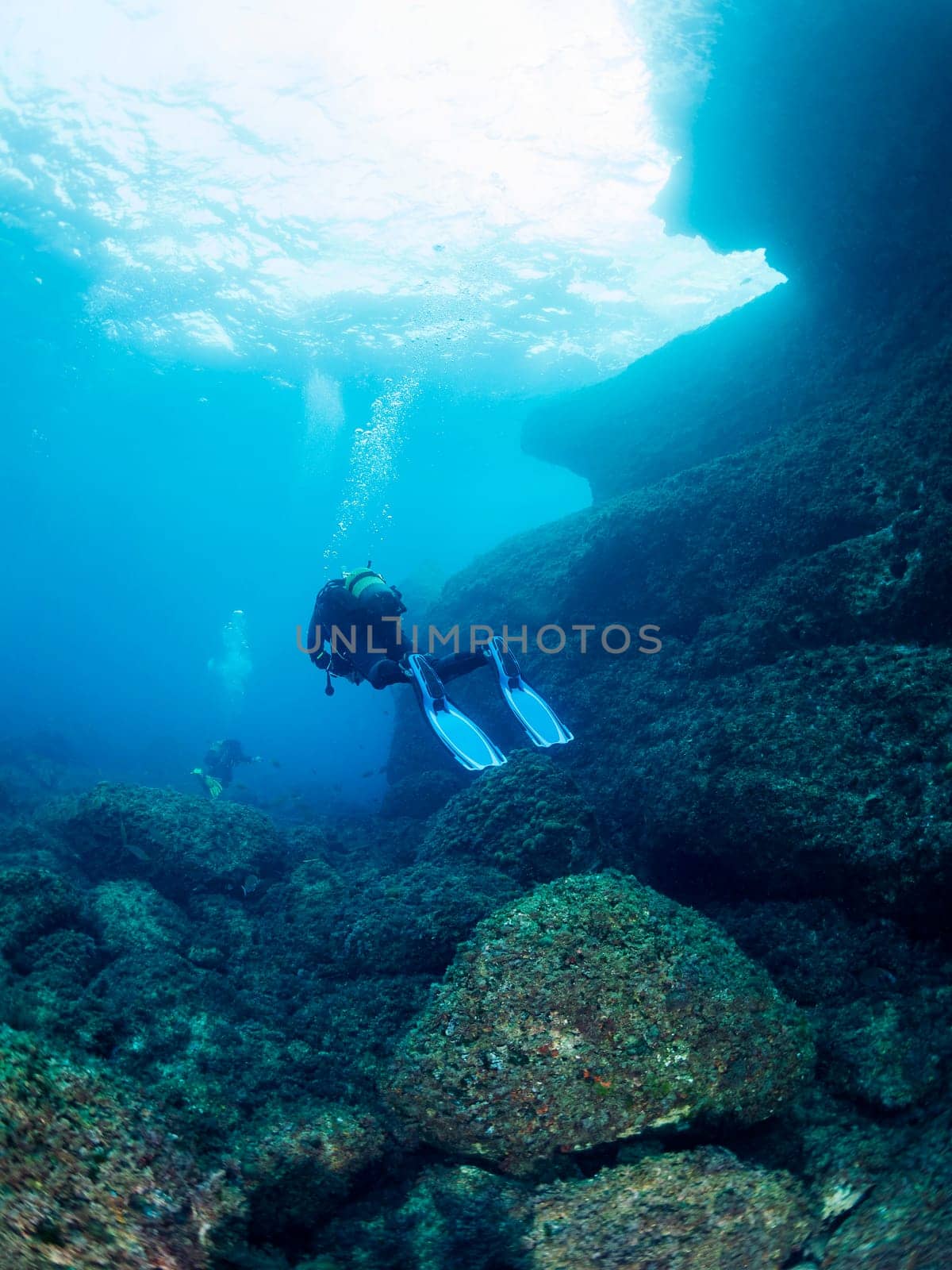 divers diving through the crystal clear water with the sun reflecting on the sea surface, concept of recreational scuba diving and underwater adventure
