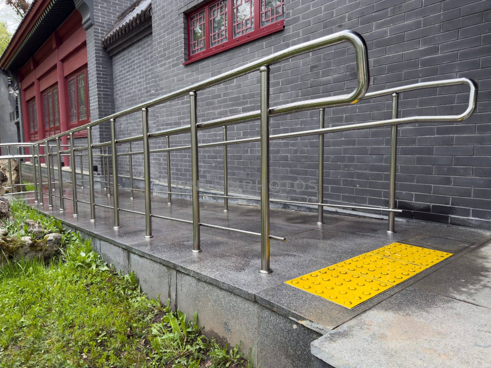 Stainless steel accessibility ramp with bright yellow tactile paving for visually impaired individuals, located next to building, highlighting inclusive design and care for people with disabilities