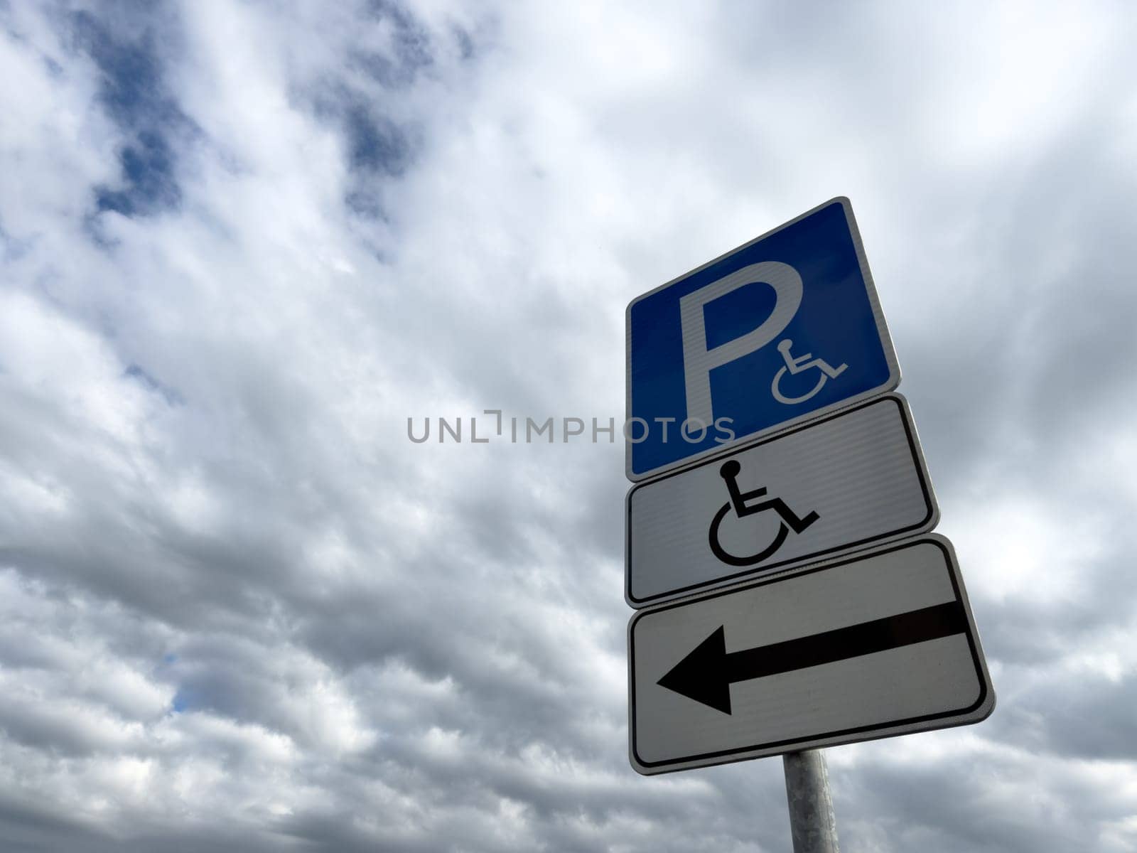 Handicap parking sign with directional arrow on cloudy day, indicating accessible parking for people with disabilities, promoting inclusion and barrier free infrastructure
