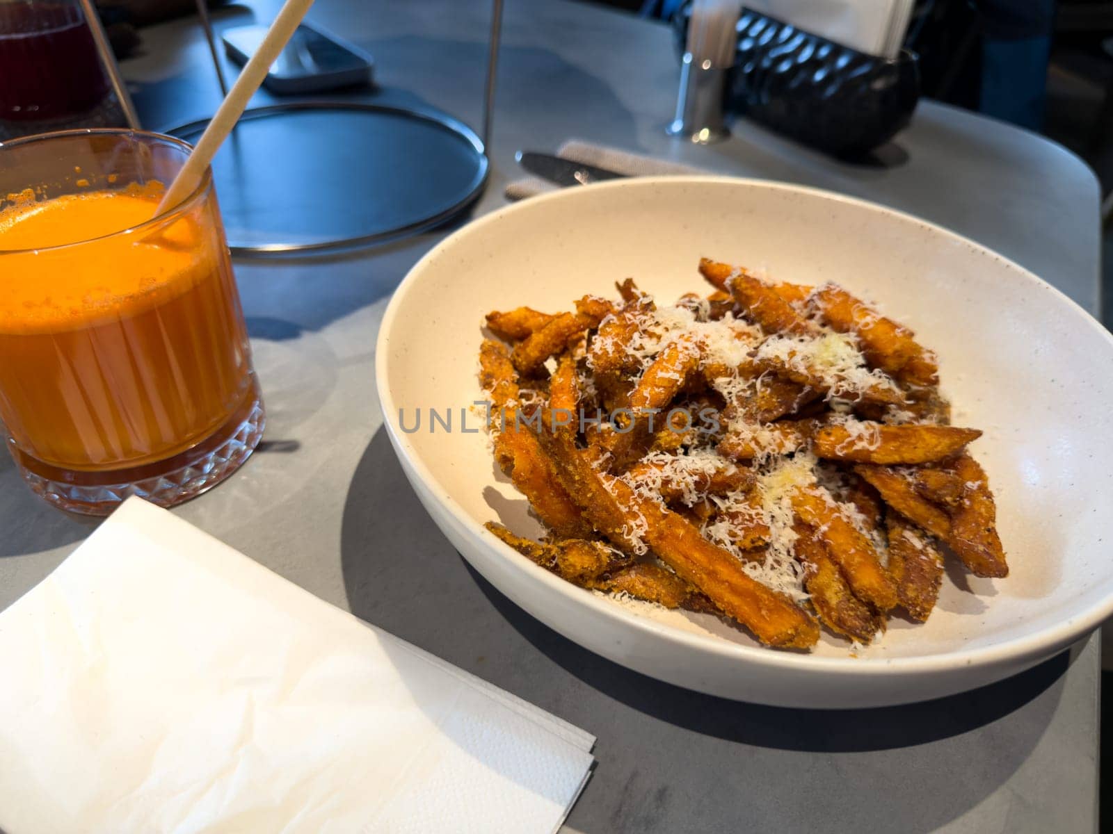 Bowl of sweet potato fries sprinkled with grated cheese served alongside a glass of fresh carrot juice. Healthy snack choice in cozy cafe, ideal for balanced and nutritious eating