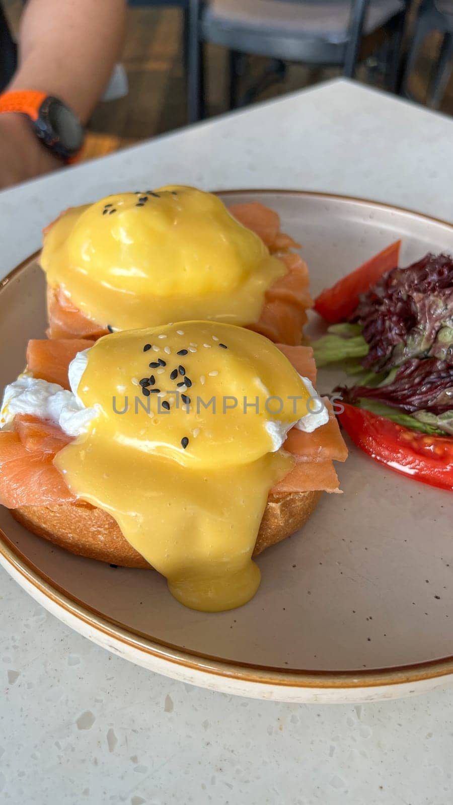 Savor a delicious brunch with this Eggs Benedict, topped with creamy hollandaise sauce and smoked salmon, served alongside a fresh side salad. Perfect for special occasions.