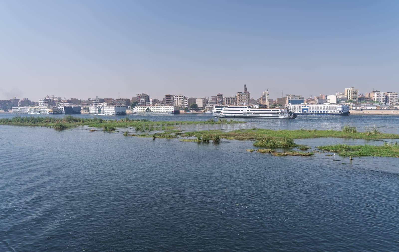 Crowded harbor in Edfu with Nile cruise boats docked and others leaving for Aswan on river in Egypt