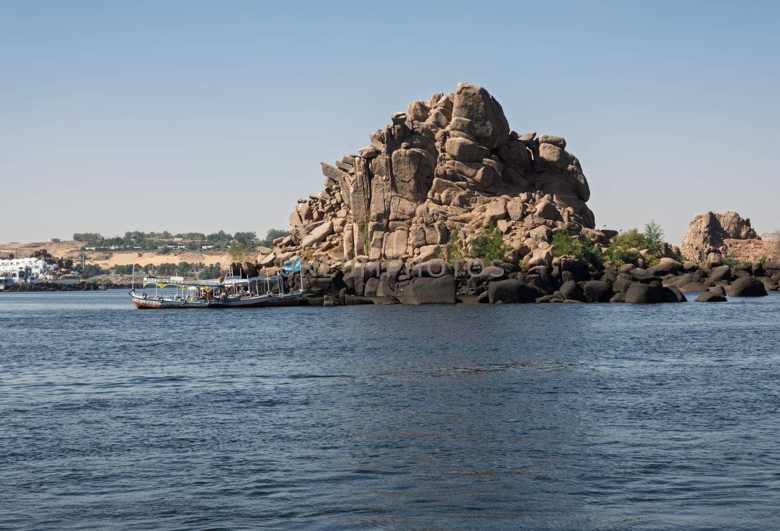 Tourists in ferry boat passing rocky island on way to Philae Temple in Aswan reservoir