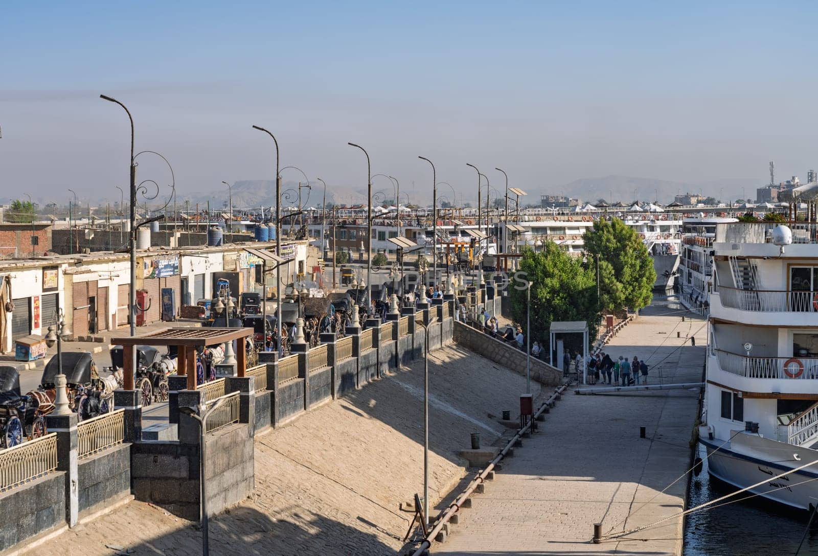 Edfu, Egypt - 6 November 2024: Cruise ships docked side by side with horses and carriages waiting in congested harbor