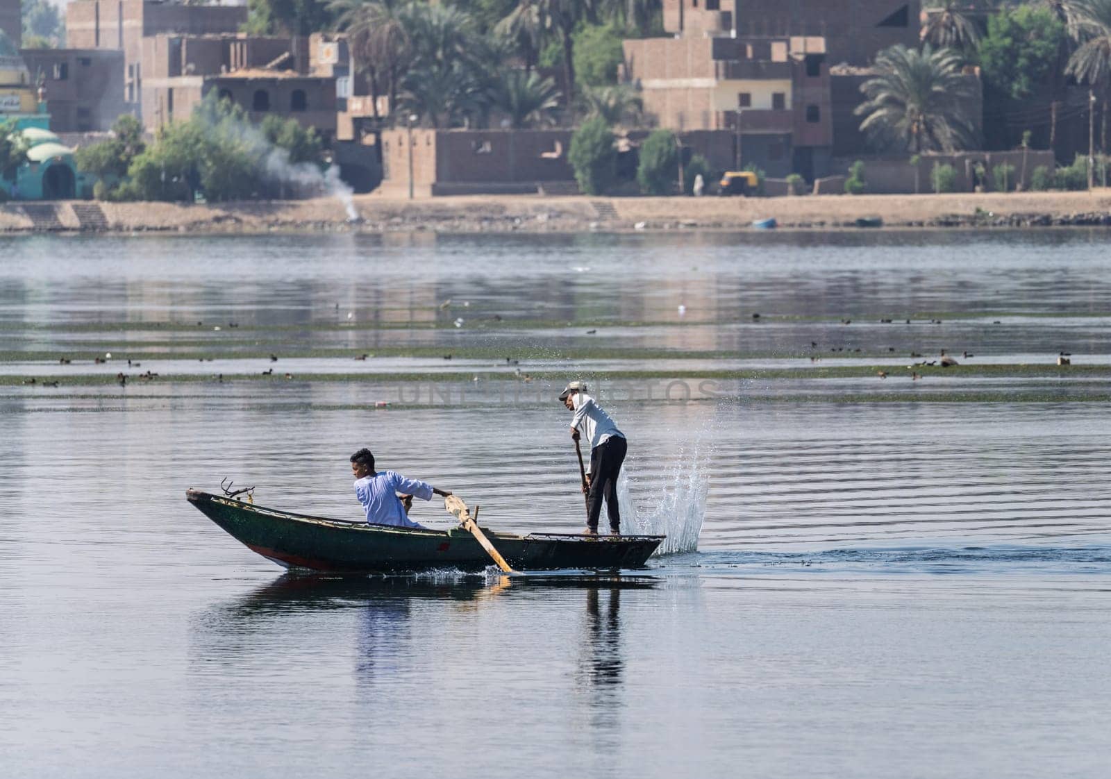 Luxor, Egypt - 1 November 2024: Two men in their small boat on a calm river Nile while tending to fishing net in the water