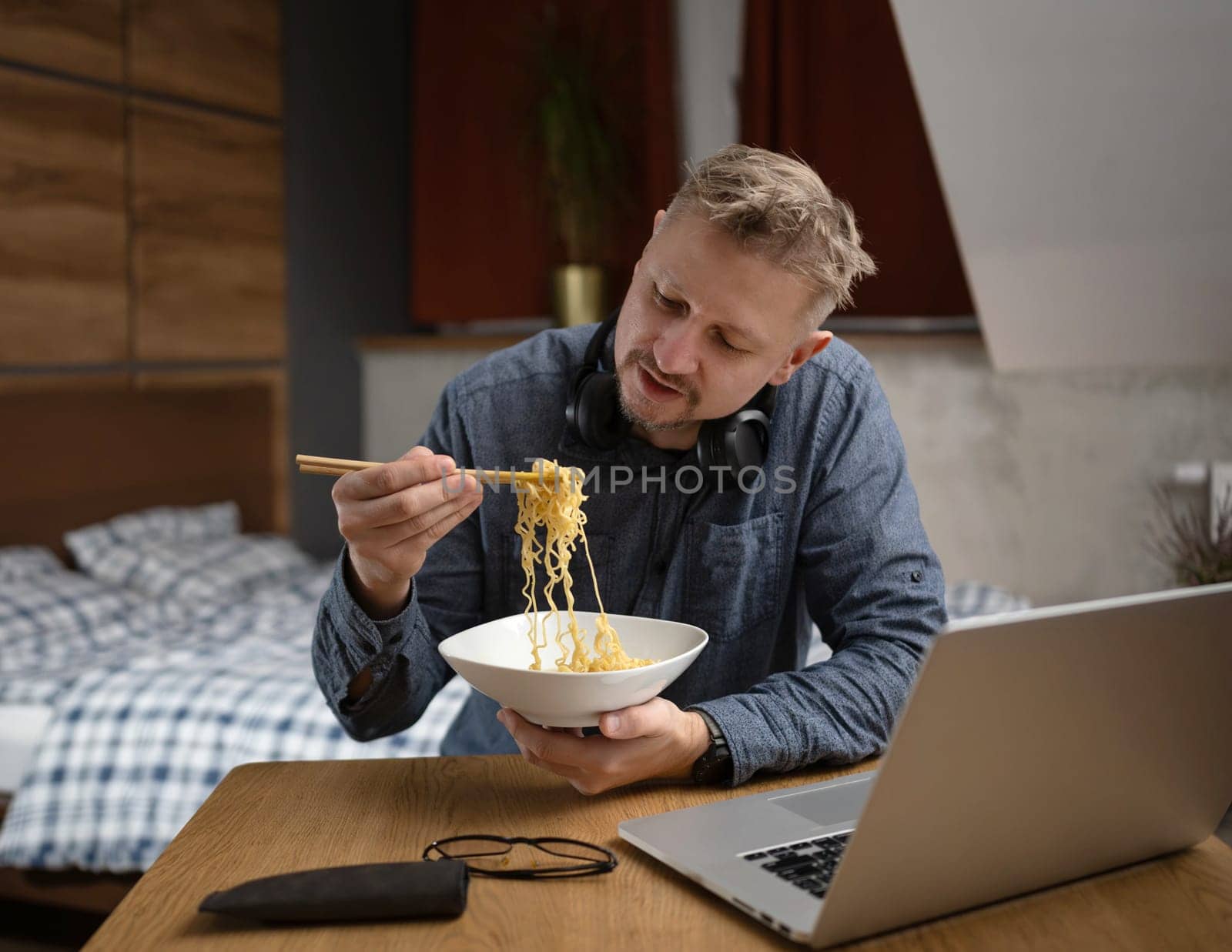 Asian Man Eating Noodles In Front Of A Laptop In Bedroom