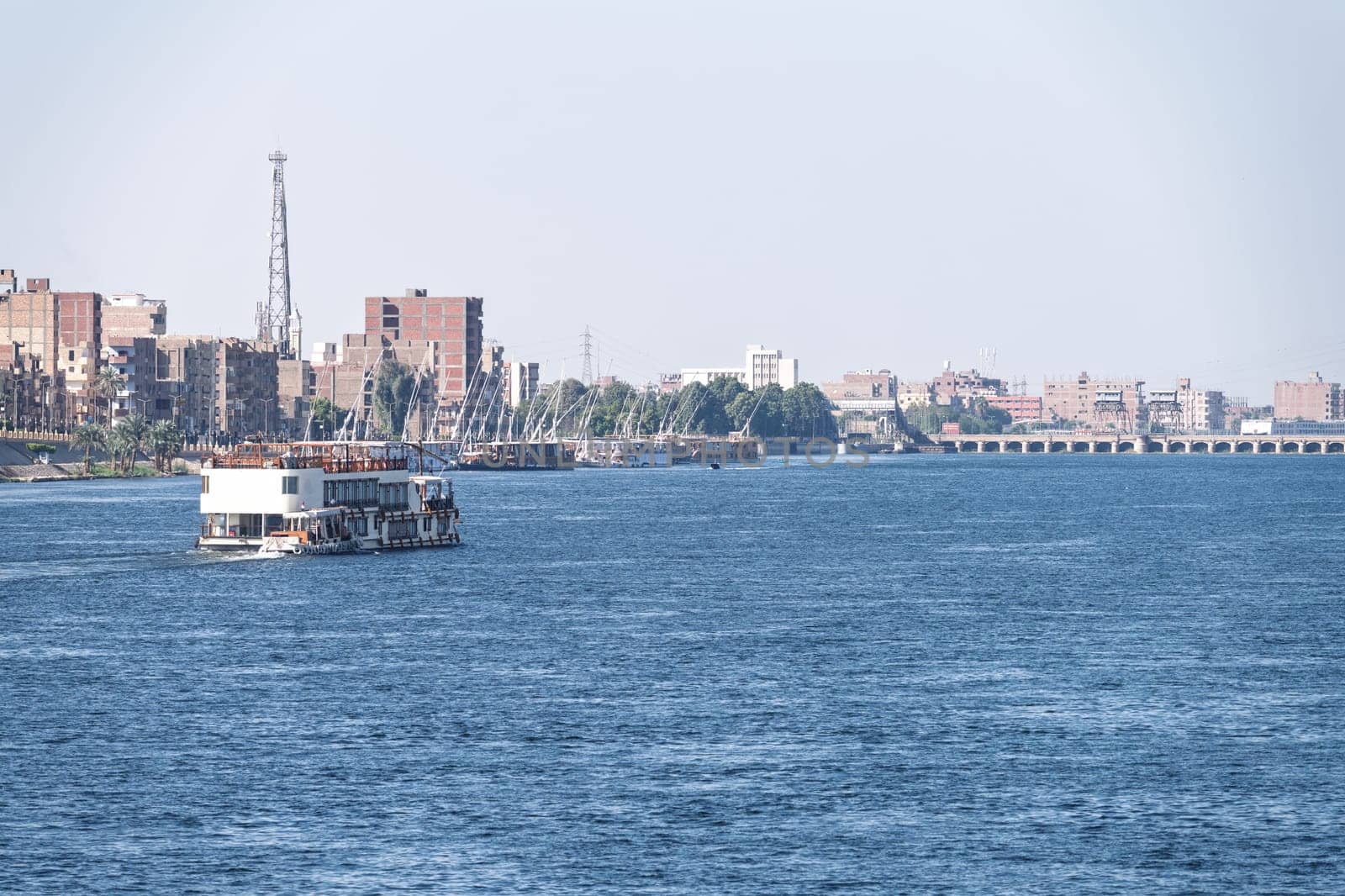 Modern waterfront buildings and dock in Esna as a Dahabiha approaches the old dam across Nile