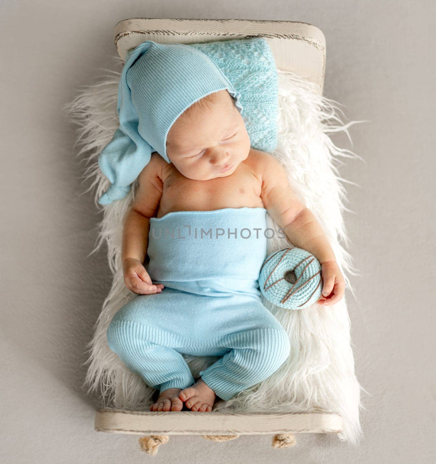 Newborn Baby Sleeping With Adorable Smile On A Little Bed In The Photo Studio
