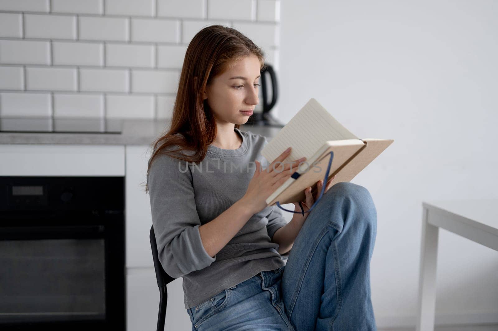 Sweet Teen Girl Reading Notebook Entries While Sitting On A Chair At Home