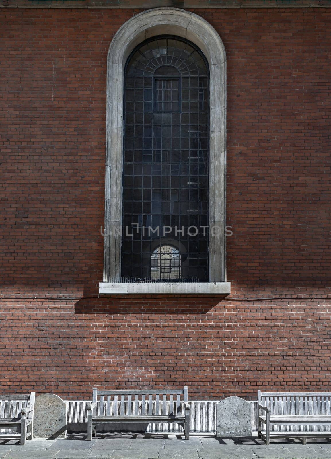 London, UK - May 13, 2025 - a view from the side of St Paul's Church is England parish church with tall glass window on red brick wall and wooden benches in Bedford Street. use it as your Wallpaper, Poster and Space for text, Selective focus.